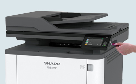 Slanted front view of the MX-B427W printer and a hand inserting a USB drive