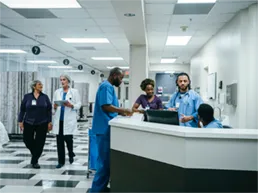 A group of hospital employees wearing scrubs gathered around a desk talking