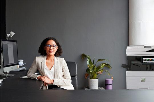 Woman sitting at a desk with a computer and a Sharp copier next to her