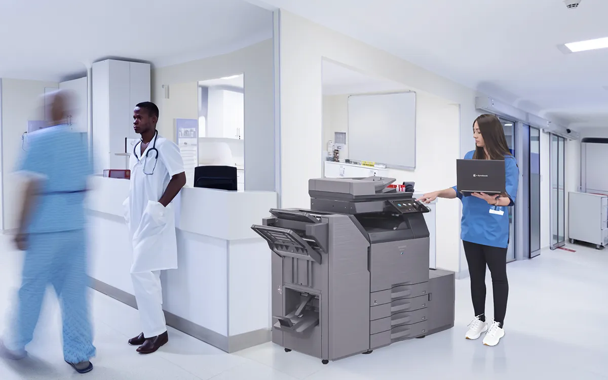 A woman using a Sharp multifunction printer in the hallway outside of a busy conference room