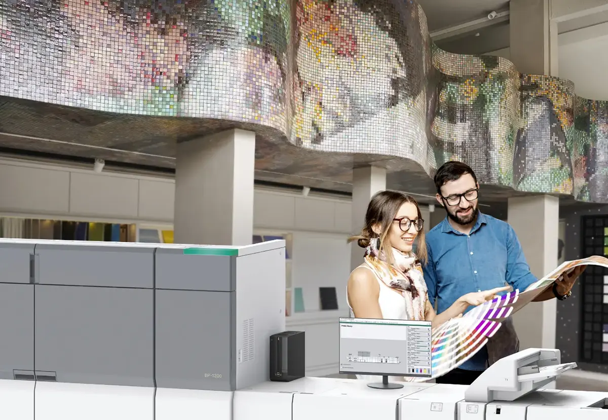 A man and a woman standing behing a Sharp Press Series Printing System reviewing prints and color swatches.