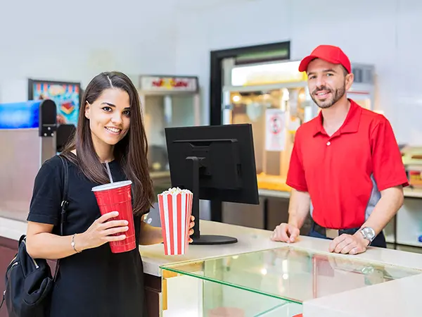 Customer holding popcorn and drink and employee at a concessions stand