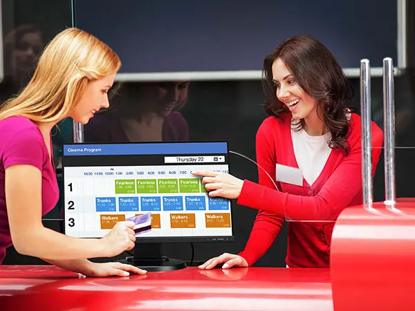 A cinema employee showing a customer movie show times on a digital display