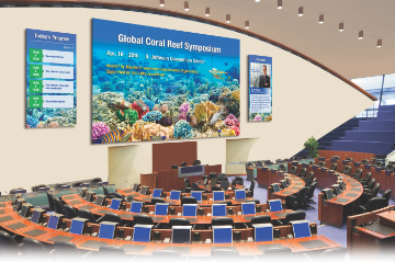 Image of a large five by five video wall display in a lecture hall auditorium showing a presentation on Coral Reefs. On both sides of the five by five video wall there are one by three video walls displaying additional coral reef presenation content