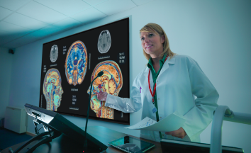 Image of a doctor presenting in front of a commercial display showing x-ray images of the human brain and side profile images of the inside of the human head anatomy