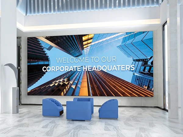 An interior view of a modern corporate lobby featuring a direct view led display that says 'WELCOME TO OUR CORPORATE HEADQUARTERS'. Two blue chairs are placed in front of the screen.