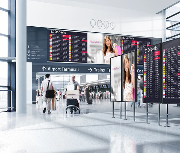 A busy airport terminal with flight departure boards displaying flight information. A smiling woman holding shopping bags is featured on a digital advertisement.