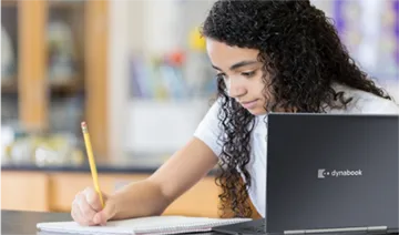Image of a young girl writing in a notebook in front of a Dynabook laptop computer
