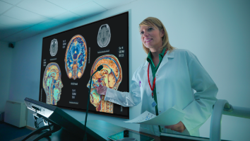 Image of doctor presenting in front of display showing images of brain scans