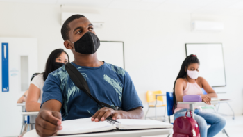 Image of a young man wearing a face mask sitting with other masked students in a classroom