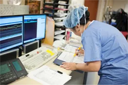 Nurse writing in a patients chart at a workstation with multiple computers