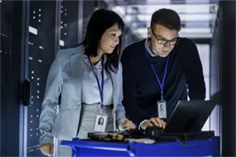 Man and woman working on a laptop in a room filled with multiple servers