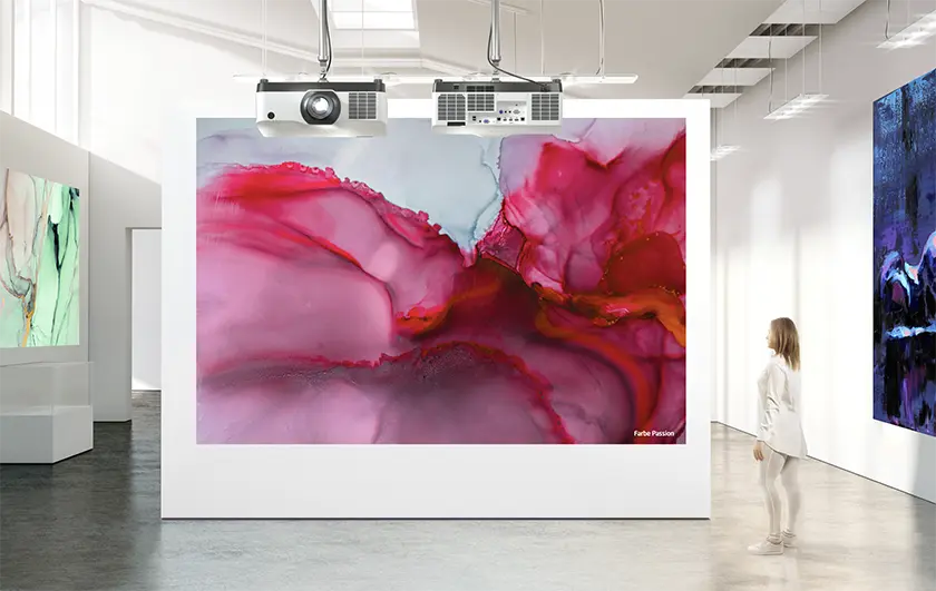 Two Laser Projectors hung from the ceiling in a modern art museum projecting artwork on a large white wall.