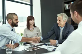 Two men shaking hands while sitting at a table with other people
