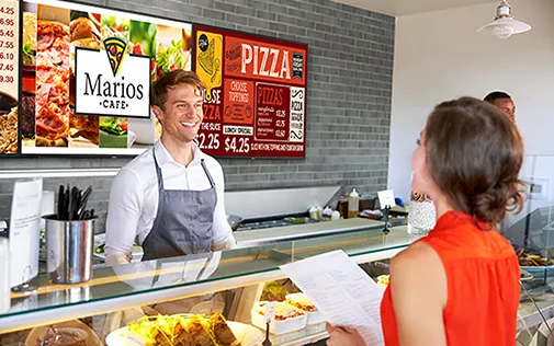 Worker behind a counter in a cafe with woman staning in front of counter holding a menu