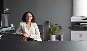 Woman sitting at a desk with a computer and a Sharp copier next to her