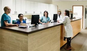 Nurses and a doctor standing around a nurse's station with computers