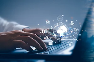A hand typing on a laptop keyboard with digital graphics of the world and icons floating above.